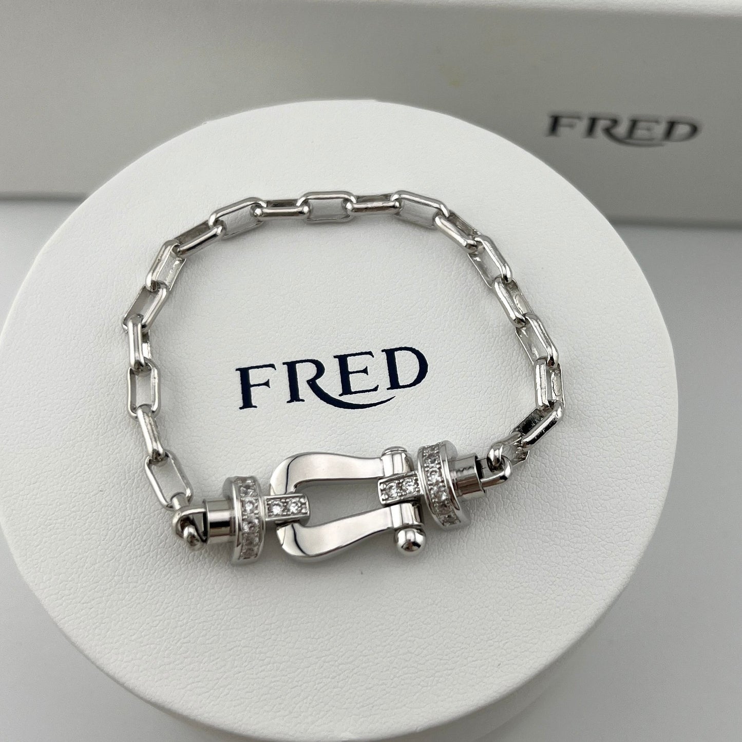 Silver bracelet with intricate design on a white stand with 'FRED' branding.