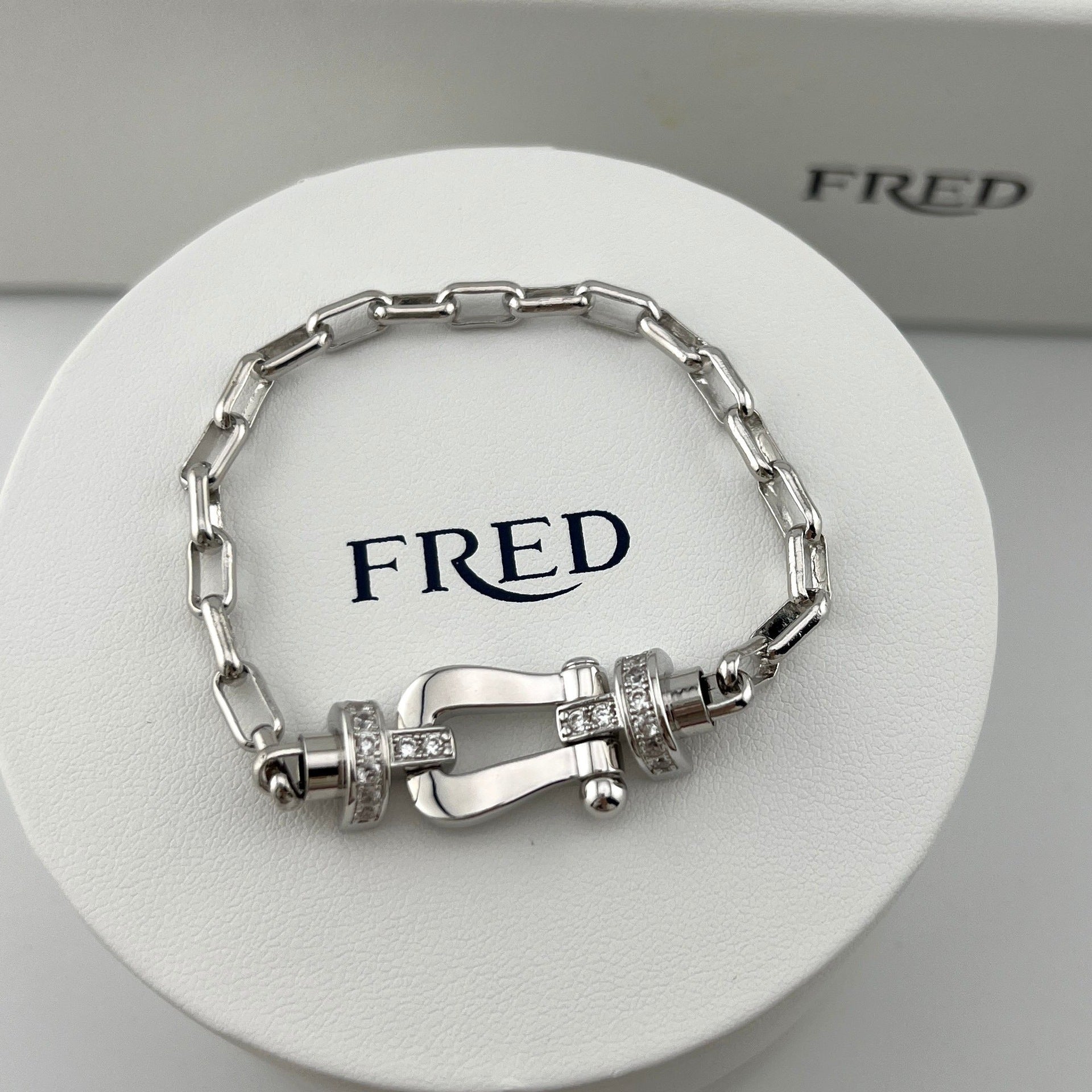 Silver bracelet with intricate design on a white stand with 'FRED' branding.