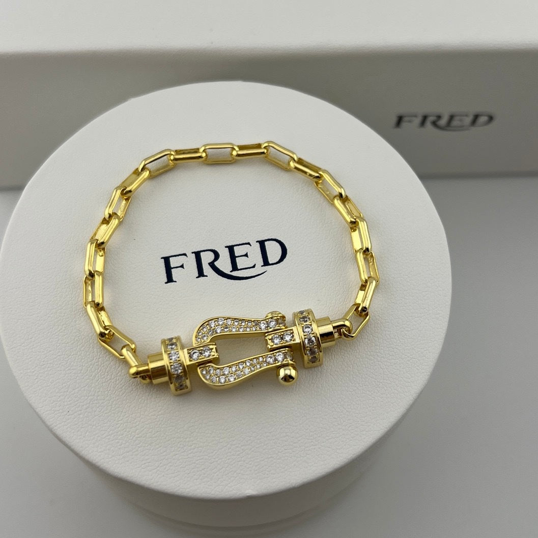 Gold bracelet with intricate design on a white stand with 'FRED' branding.