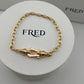 Gold bracelet on a white circular stand with 'FRED' branding.