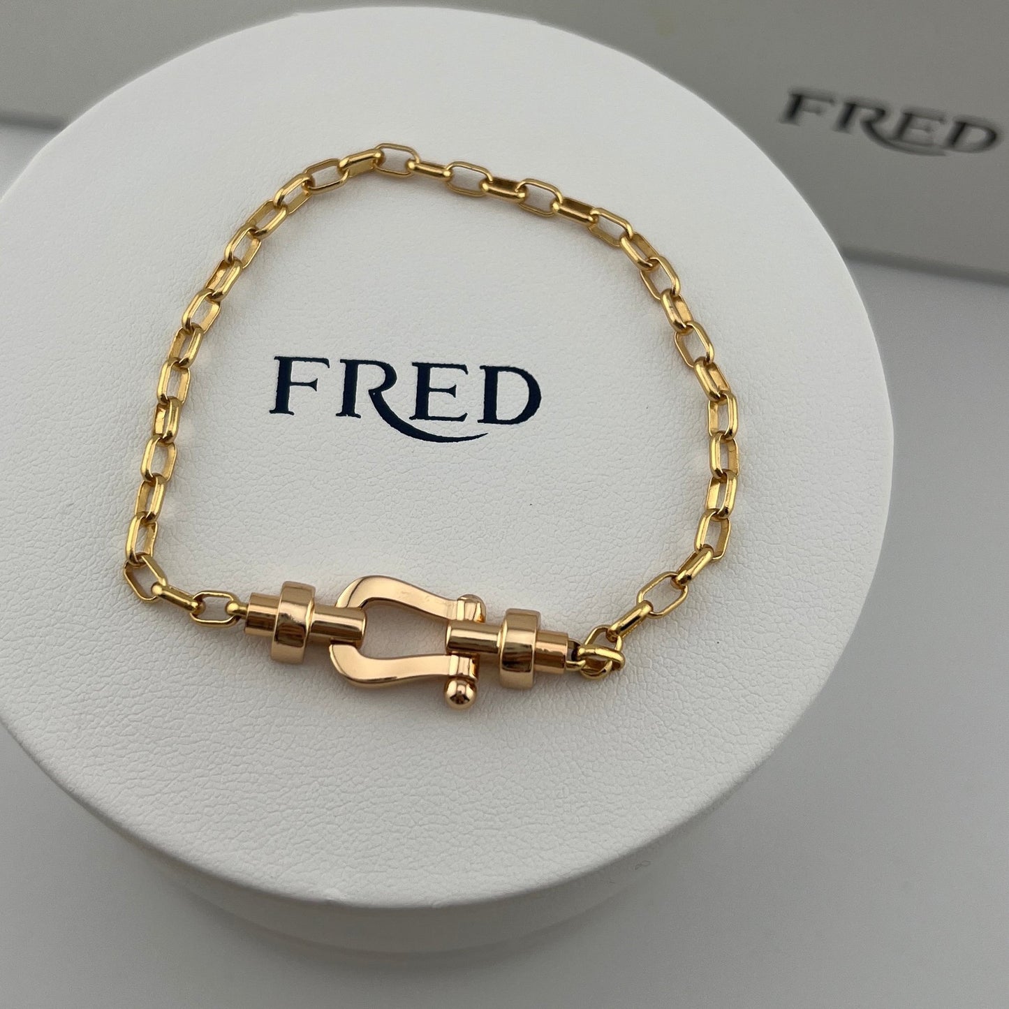 Gold bracelet on a white circular stand with 'FRED' branding.