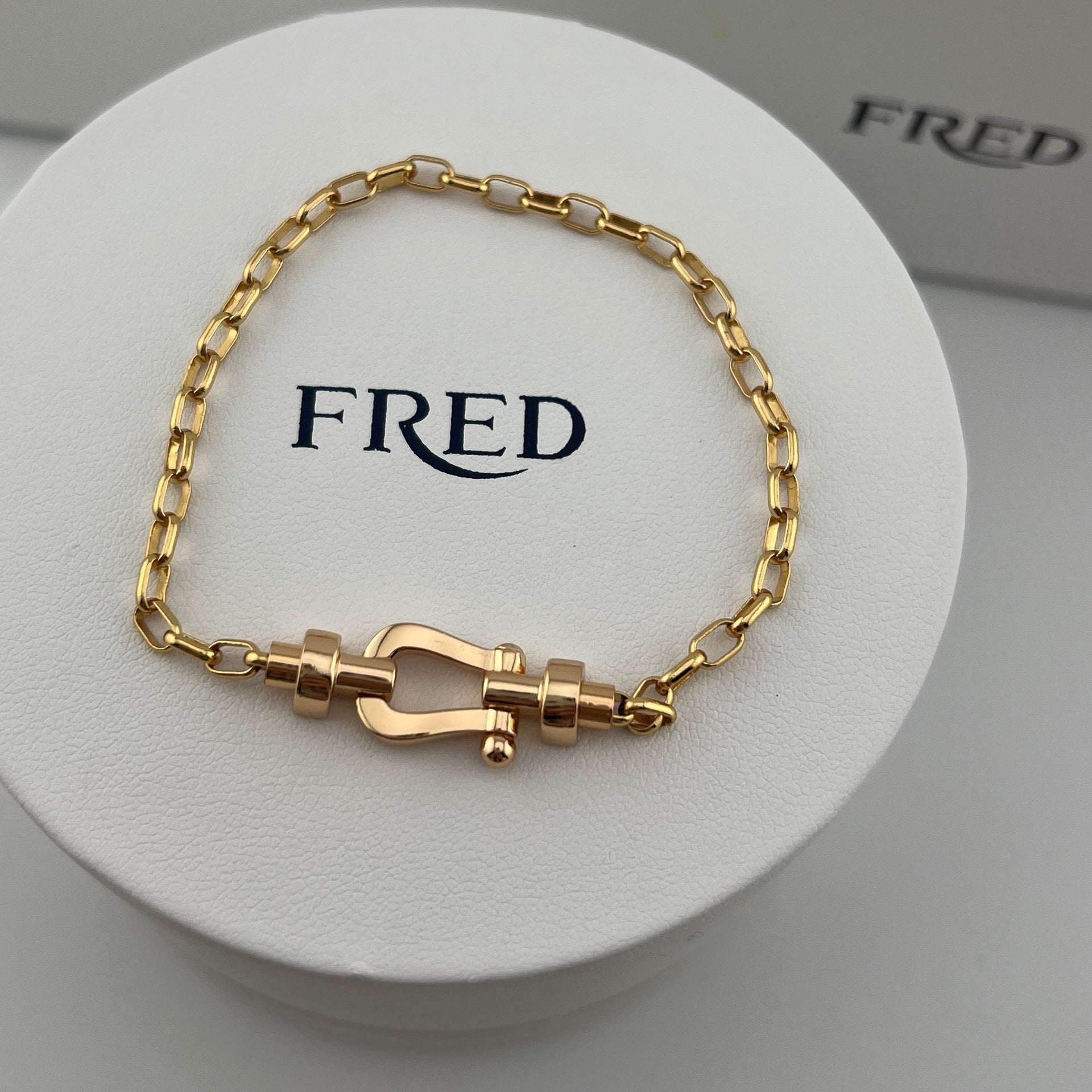 Gold bracelet on a white circular stand with 'FRED' branding.