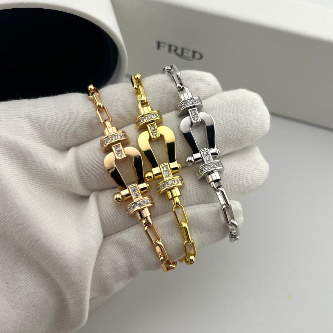 Three gold and silver bracelets on a white cloth with 'FRED' branding.