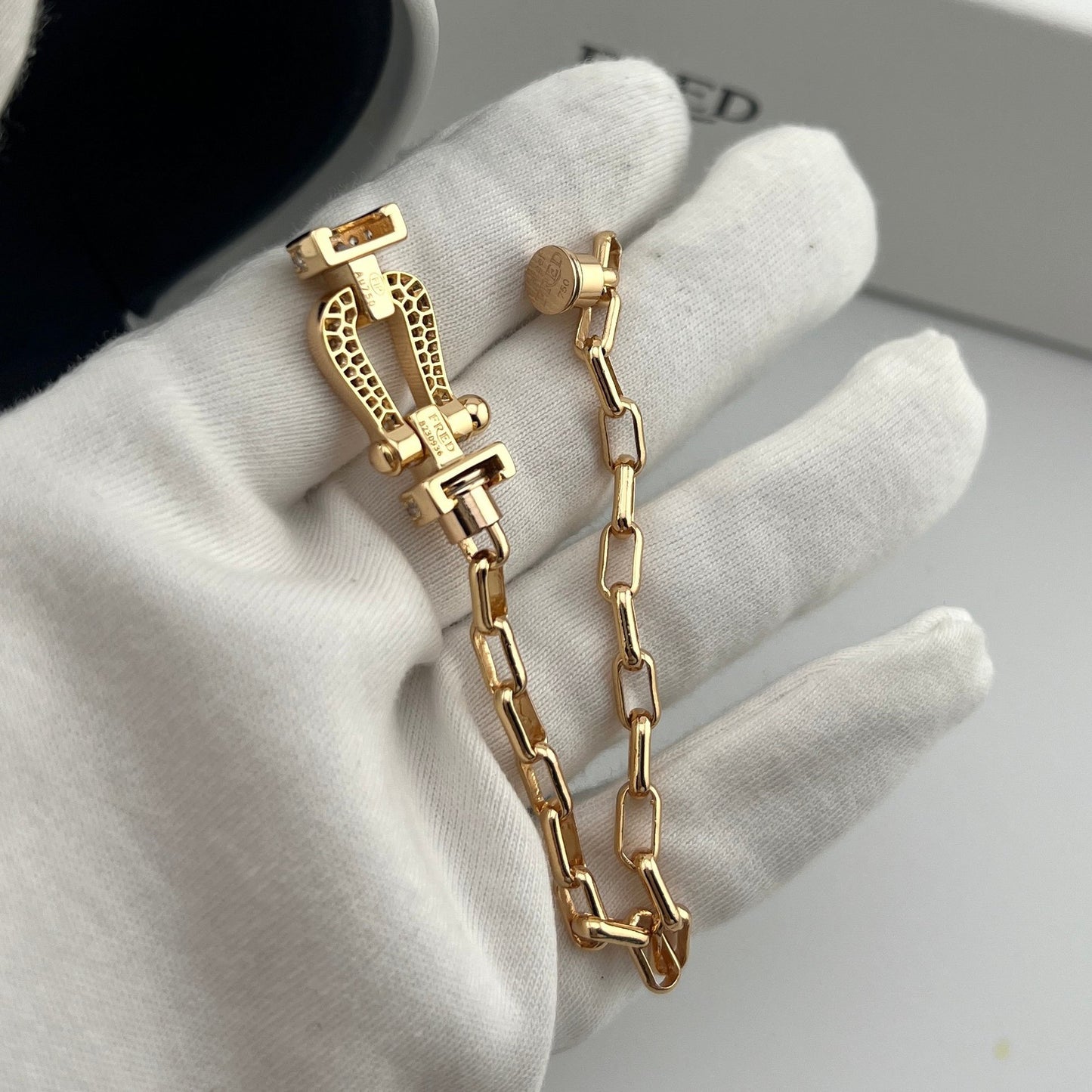 Gold chain bracelet held by a gloved hand on a neutral background