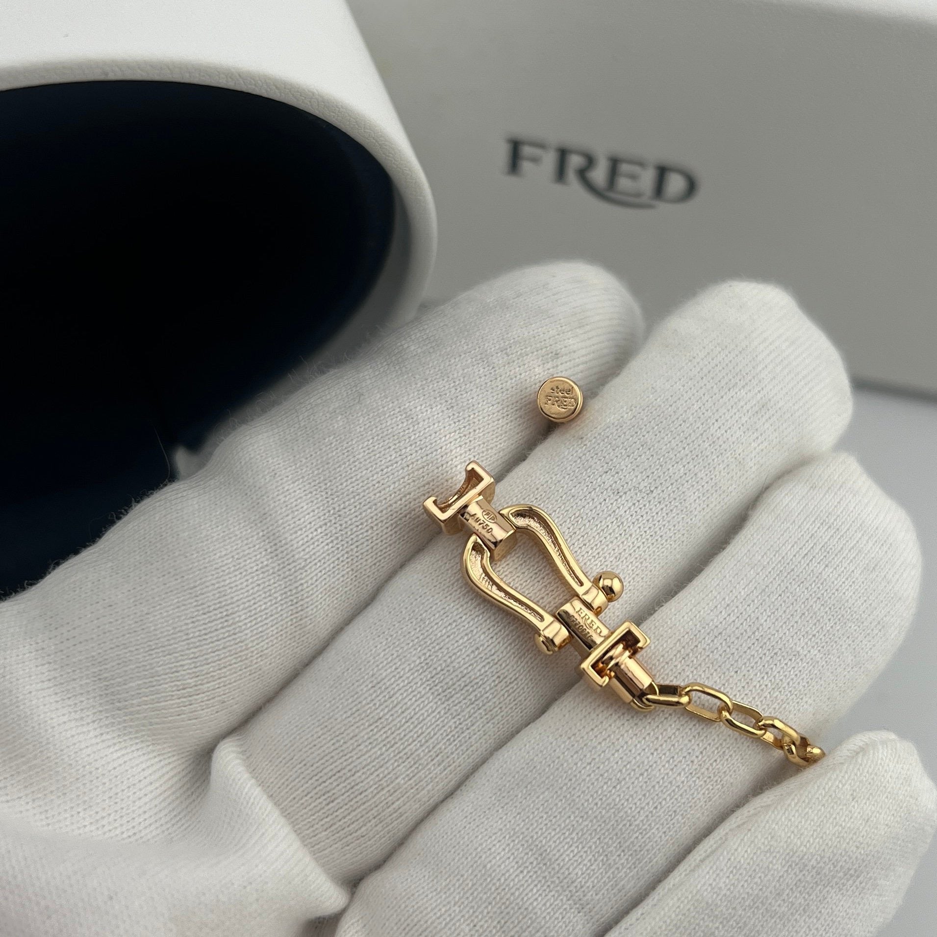 Gold bracelet and earring set on a white glove with 'FRED' branding in the background.