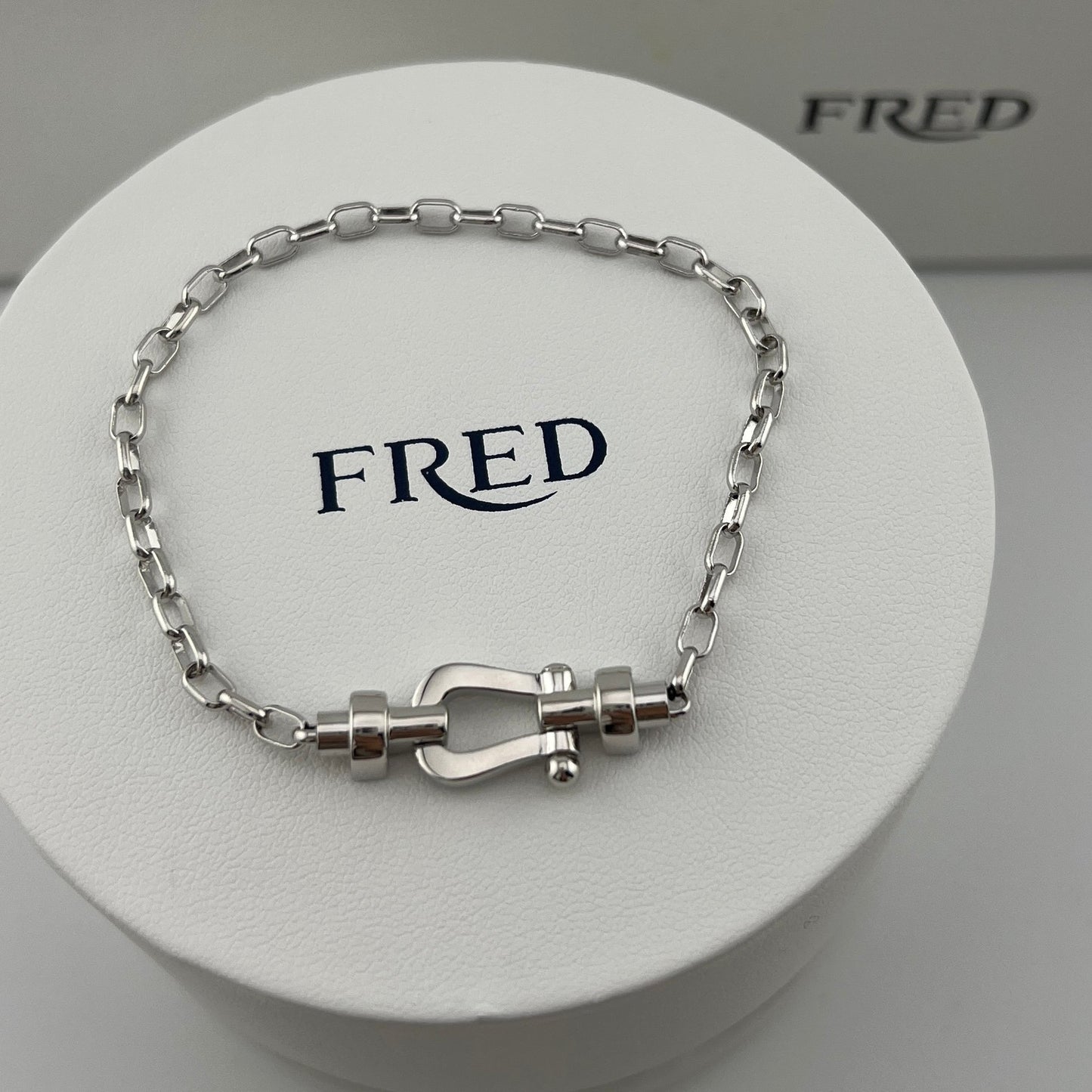Silver bracelet with clasp on a white display stand with 'FRED' branding.
