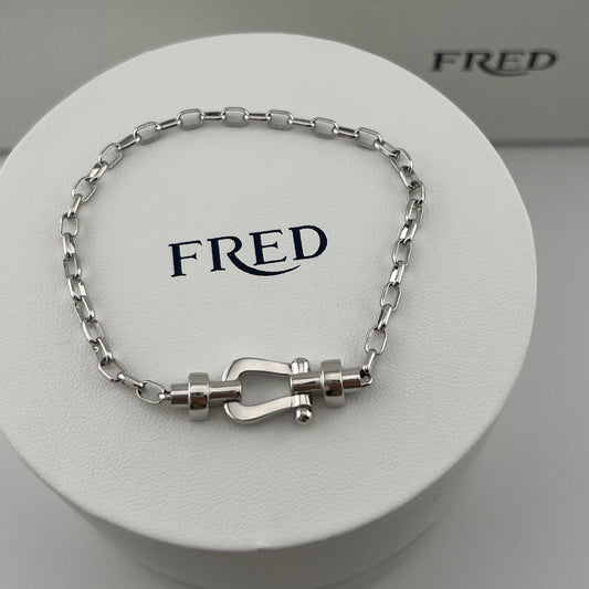 Silver bracelet with clasp on a white display stand with 'FRED' branding.