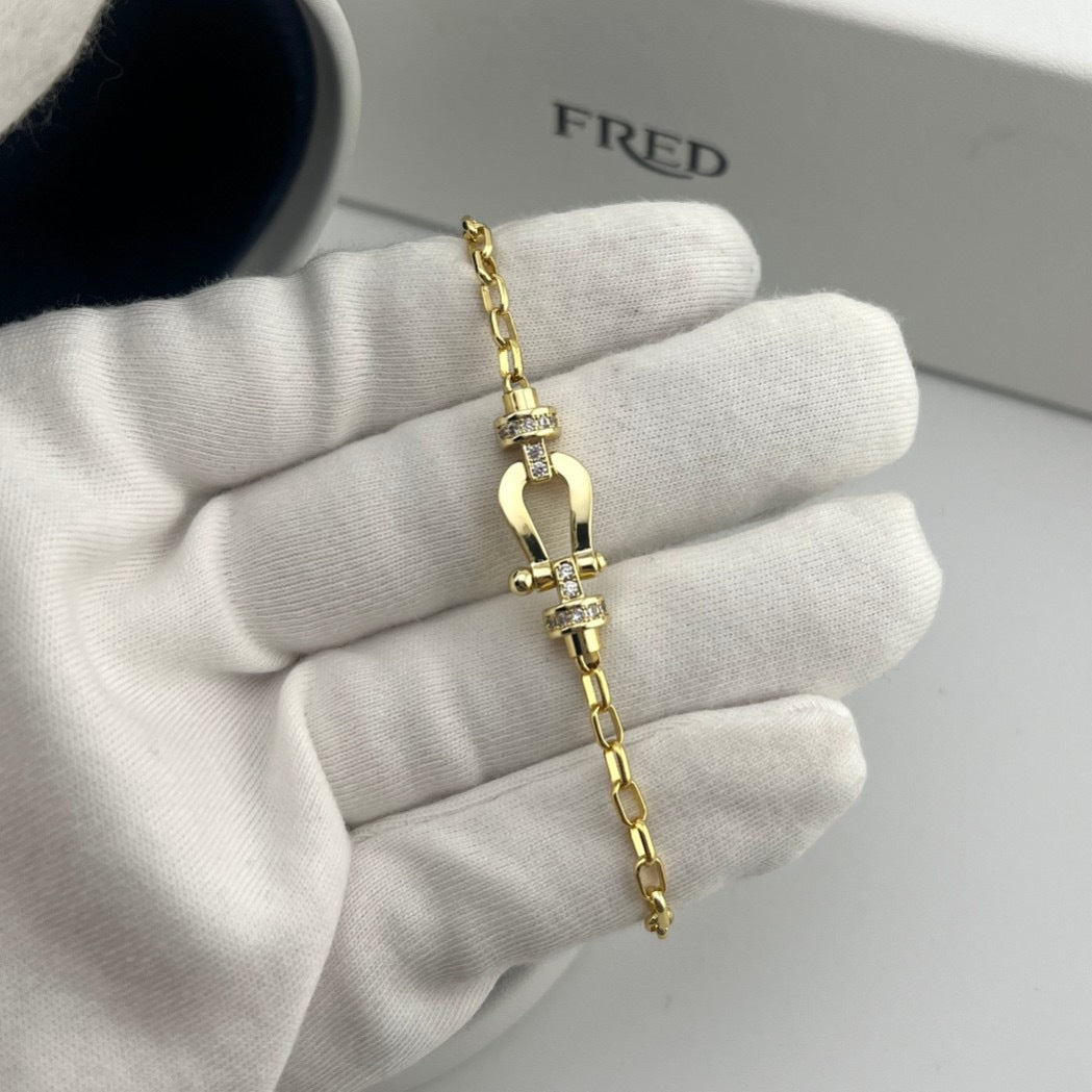 Gold bracelet on a hand wearing a white glove with 'FRED' branding in the background.