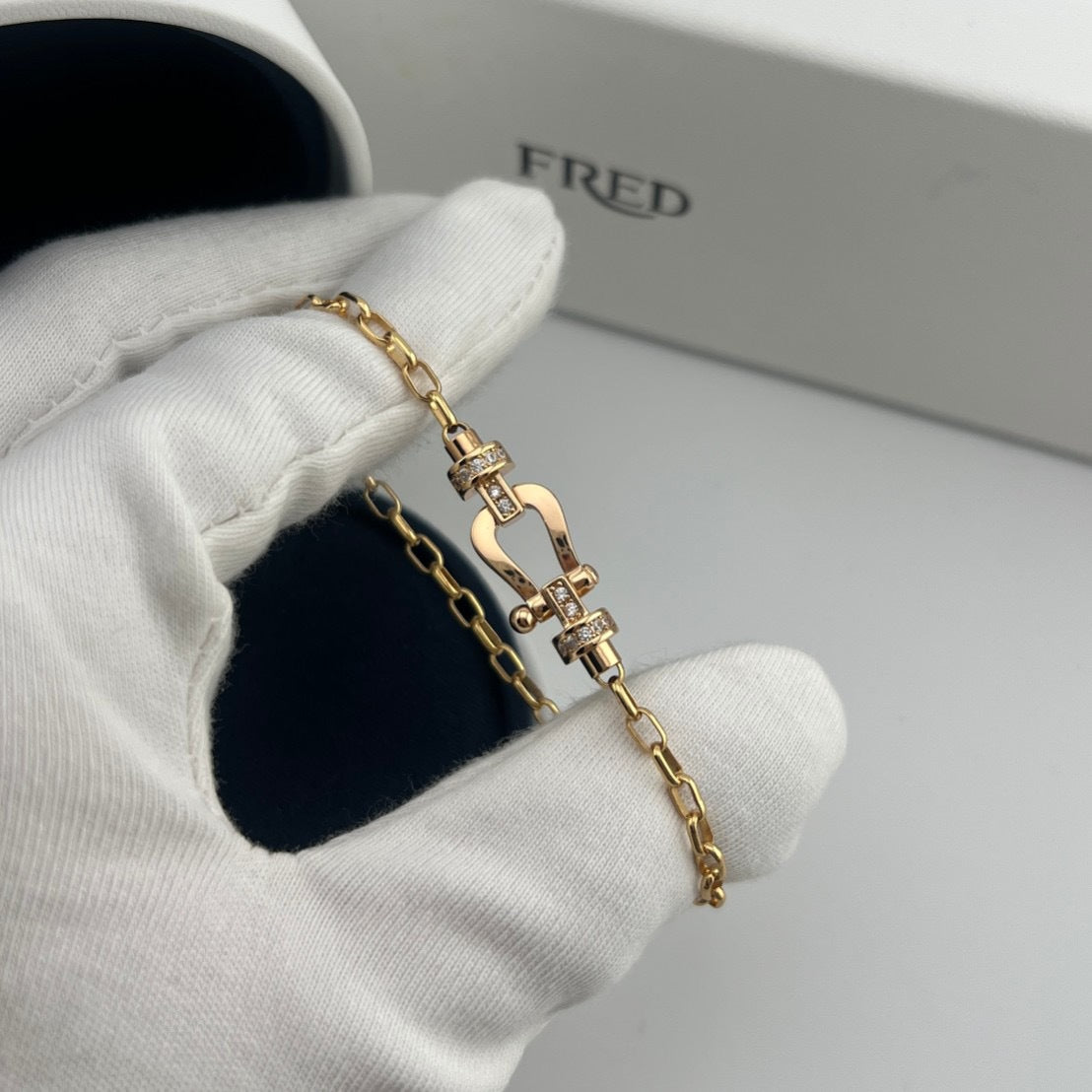 Gold bracelet held by a gloved hand with 'FRED' branding in the background