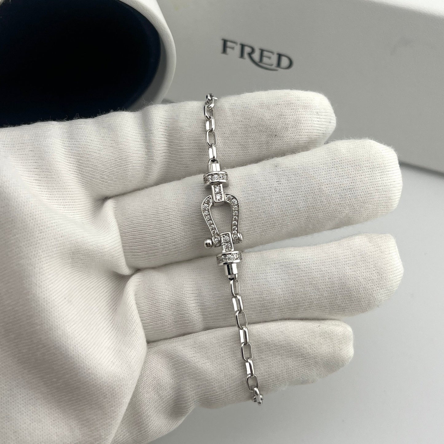 Silver bracelet on a gloved hand with 'FRED' branding in the background