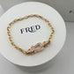 Gold bracelet with a clasp on a white stand featuring the brand 'FRED'.