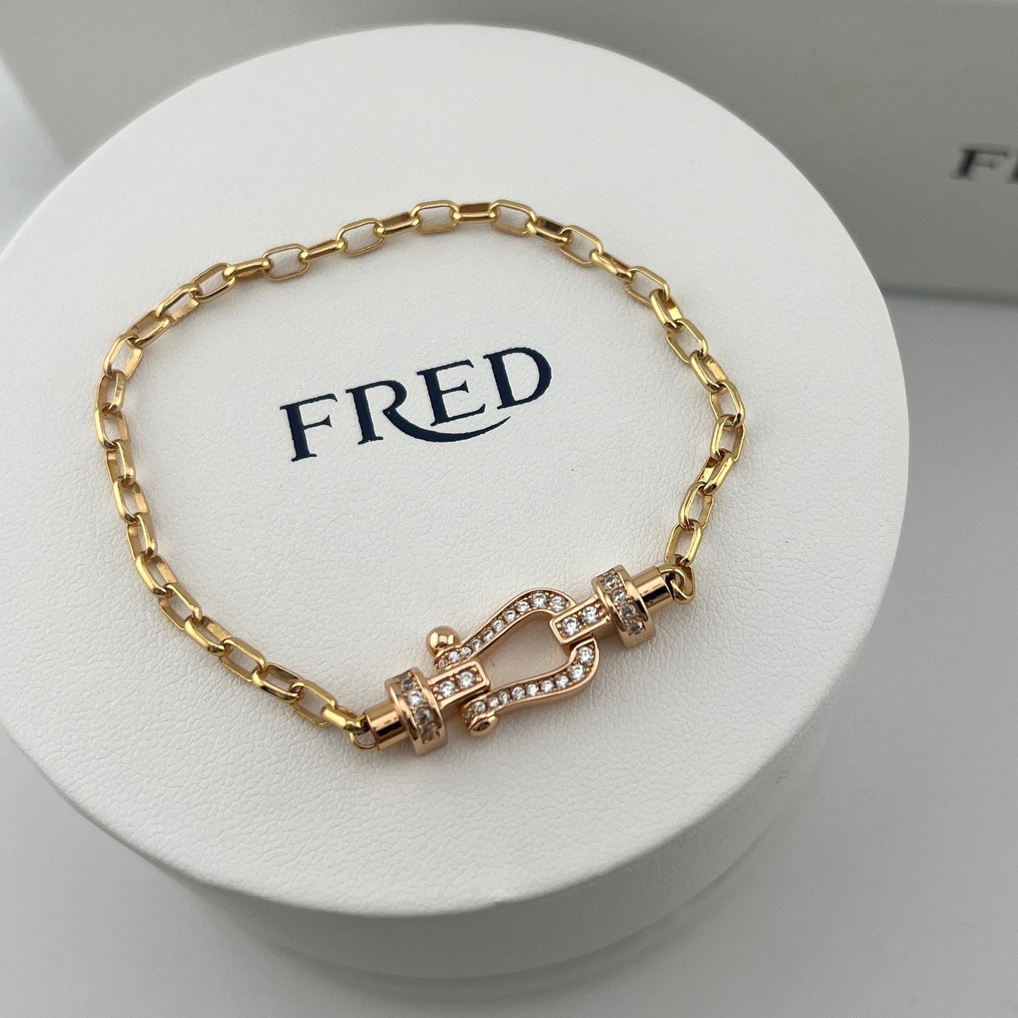 Gold bracelet with a clasp on a white stand featuring the brand 'FRED'.