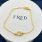 Gold bracelet with a decorative clasp on a white circular stand with 'FRED' branding.