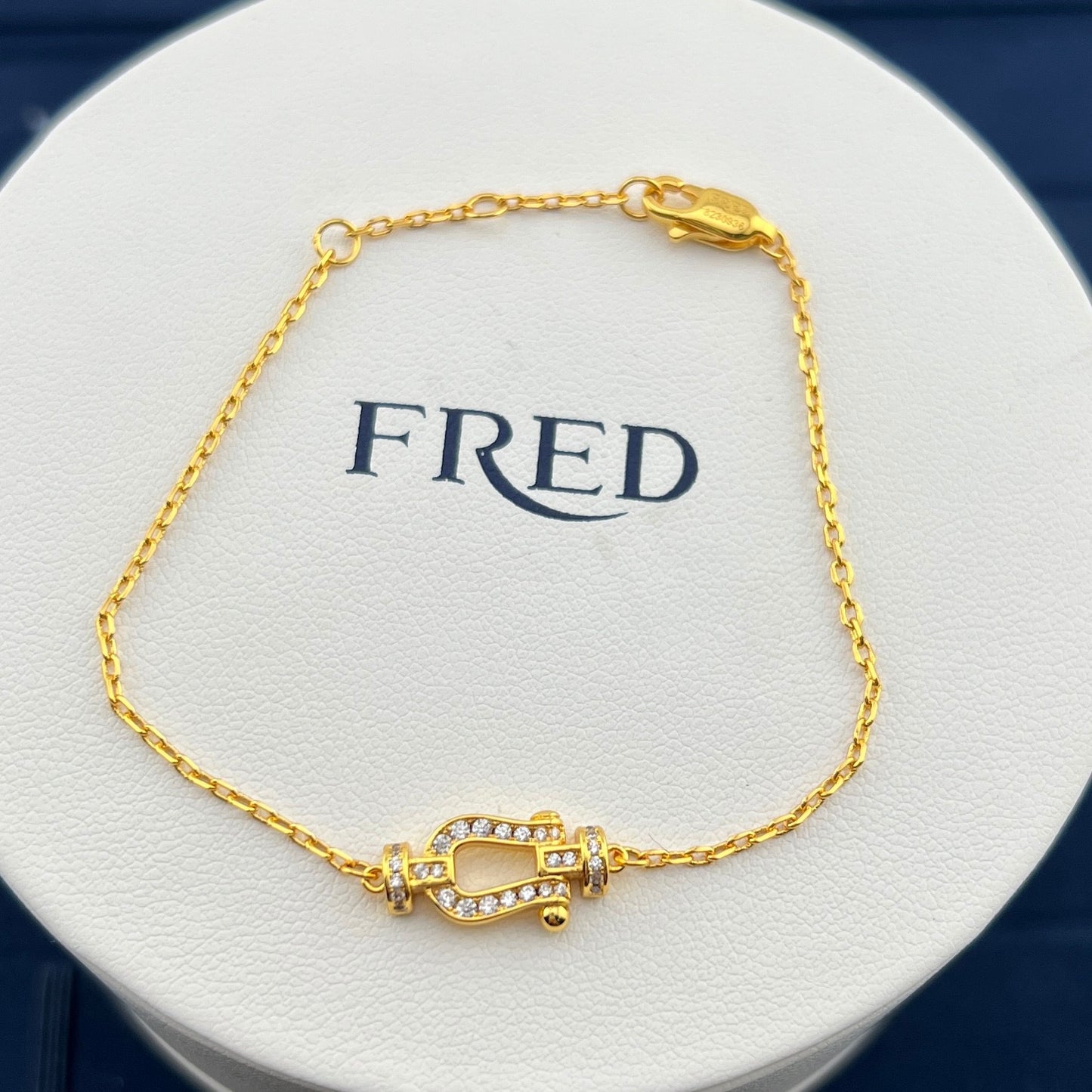 Gold bracelet with a decorative clasp on a white circular stand with 'FRED' branding.