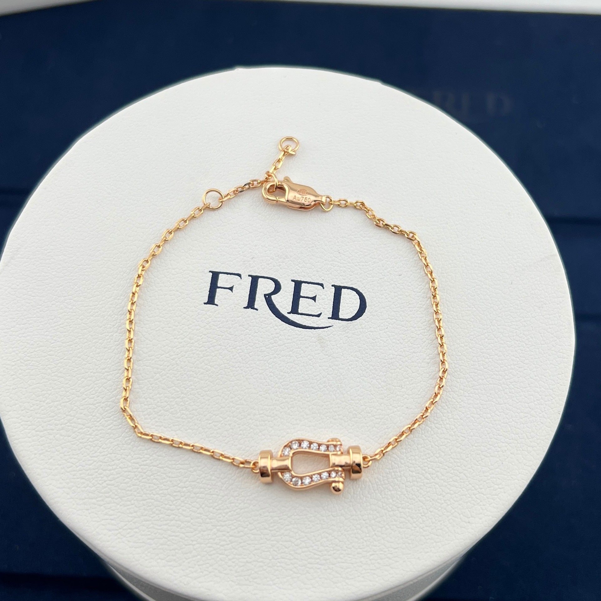 Gold bracelet on a white circular box with 'FRED' branding.