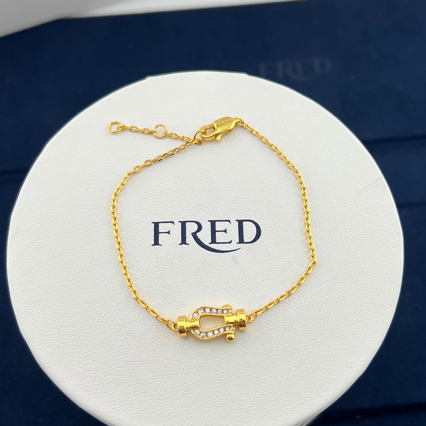 Gold bracelet on a white display card with 'FRED' branding.