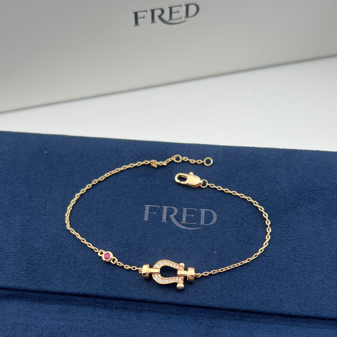 Gold bracelet with a clasp on a blue FRED branded surface