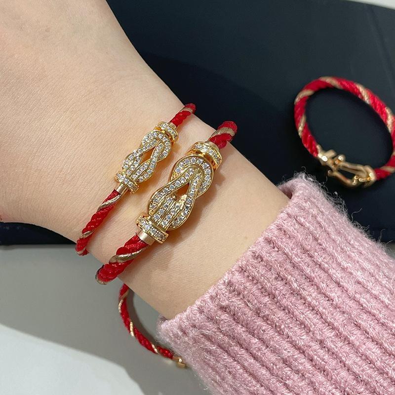 Force 10 bracelet 18k yellow gold and diamonds  with red cord and gold accents on a wrist, with a pink sleeve.