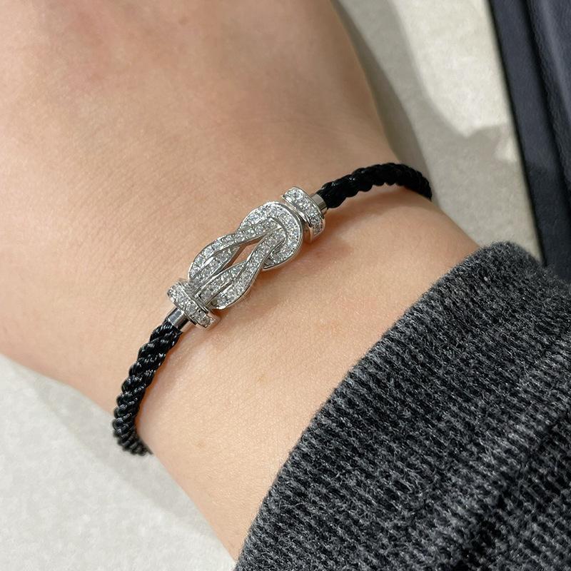 Force 10 bracelet 18k yellow gold and diamonds with black cord and silver clasp on a wrist, wearing a gray sweater.