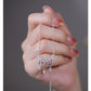 Hand holding a silver necklace with a detailed pendant against a neutral background
