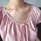 Person wearing a pink top and a silver necklace with a floral pendant.