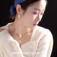Woman wearing a blue headband and white sweater with jewelry, against a black background.