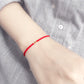 Red string bracelet on a wrist with a gray shirt background