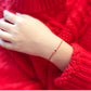 Hand wearing a red bracelet on a red textured fabric backgroundBracelet with red and gold braided design and a square gemstone on a white background