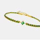 Gold and green braided bracelet with a green gemstone on a light gray background