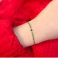 Gold bracelet with green stones on a wrist against a red fabric background