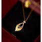 Gold necklace with a leaf-shaped pendant on a dark surface