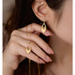 Gold earrings being worn with a hand holding one of them close to the ear.