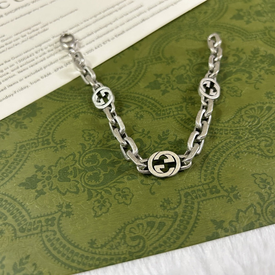Silver chain bracelet with Gucci logo on a green patterned fabric background