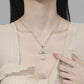 Person wearing a gold cross necklace with a green gemstone, pointing at it.