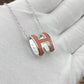High-End “H” Enamel Pendant Necklace Silver and brown pendant necklace on a light gray fabric background