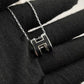 High-End “H” Enamel Pendant Necklace Silver necklace with a letter 'H' pendant on a black fabric background