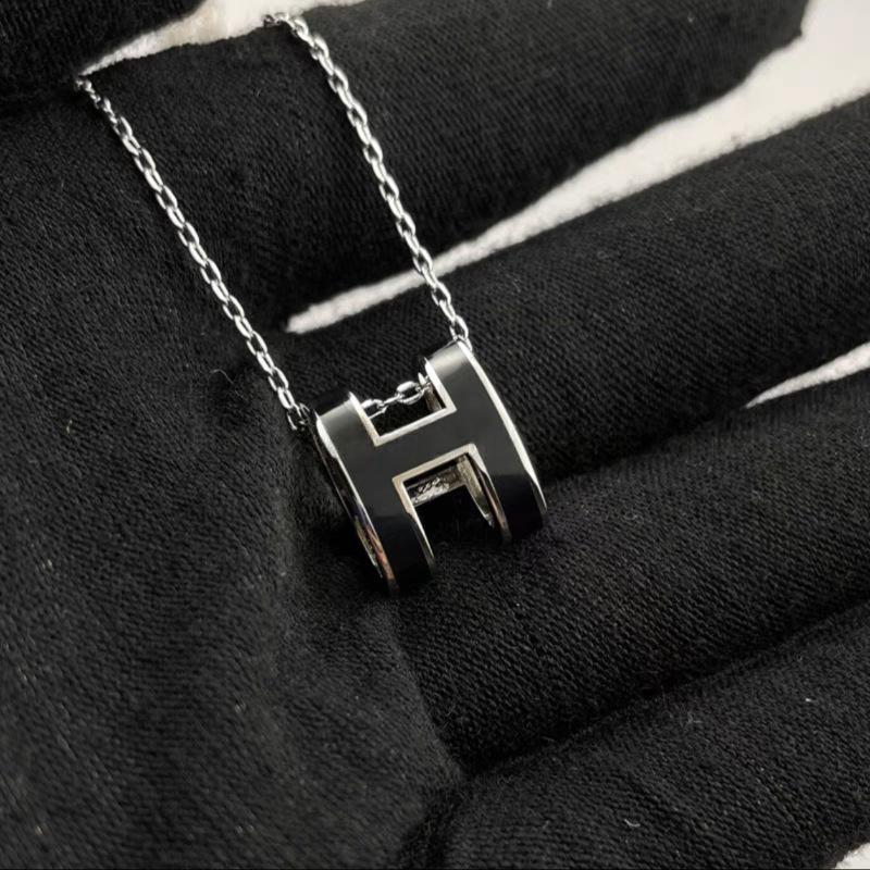 High-End “H” Enamel Pendant Necklace Silver necklace with a letter 'H' pendant on a black fabric background