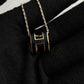 High-End “H” Enamel Pendant Necklace Black and gold necklace with a geometric pendant on a black fabric background