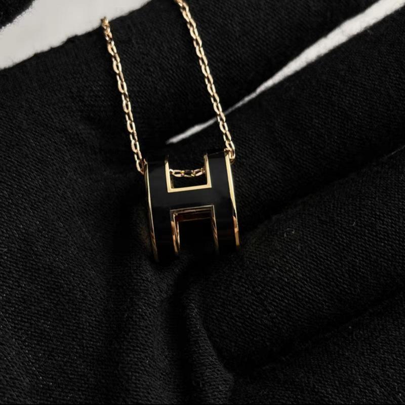 High-End “H” Enamel Pendant Necklace Black and gold necklace with a geometric pendant on a black fabric background