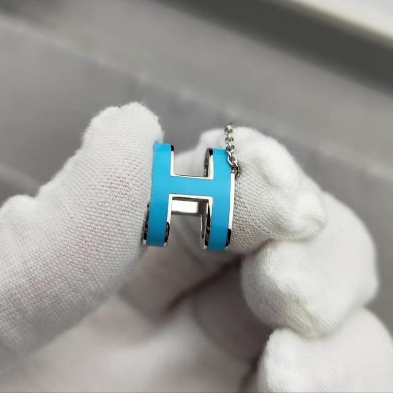High-End “H” Enamel Pendant Necklace Necklace with a blue 'H' pendant held by a gloved hand against a neutral background