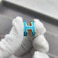 High-End “H” Enamel Pendant Necklace Gold and blue earring held by a gloved hand on a neutral background