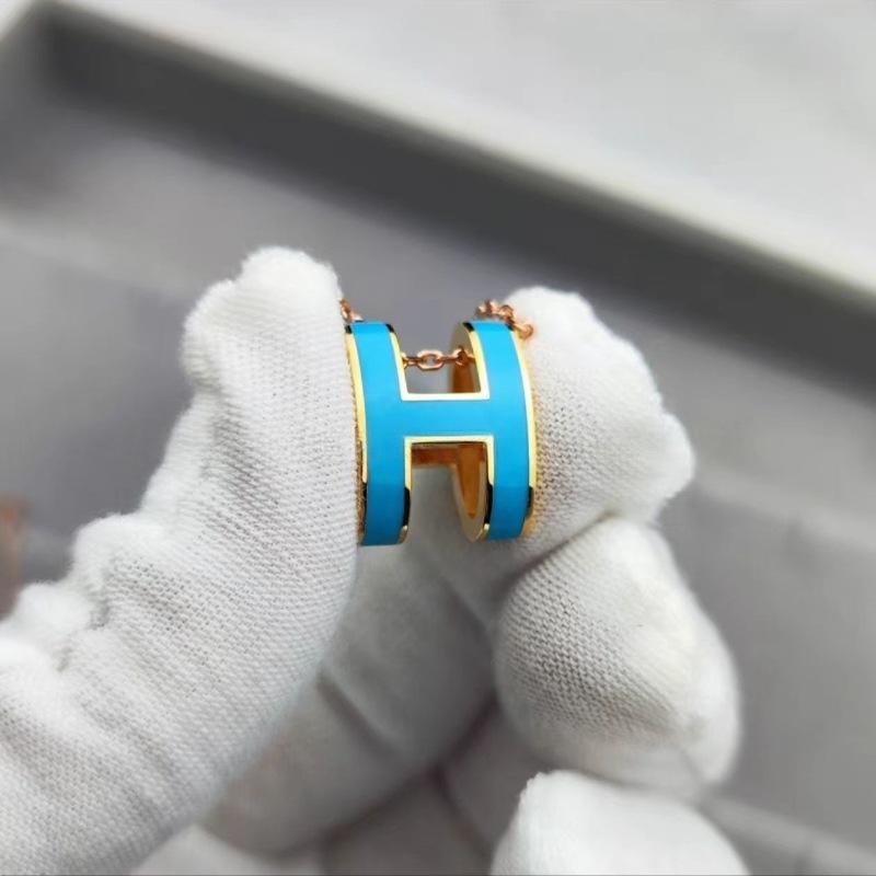 High-End “H” Enamel Pendant Necklace Gold and blue earring held by a gloved hand on a neutral background