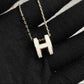 High-End “H” Enamel Pendant Necklace Necklace with a white 'H' pendant on a black fabric background