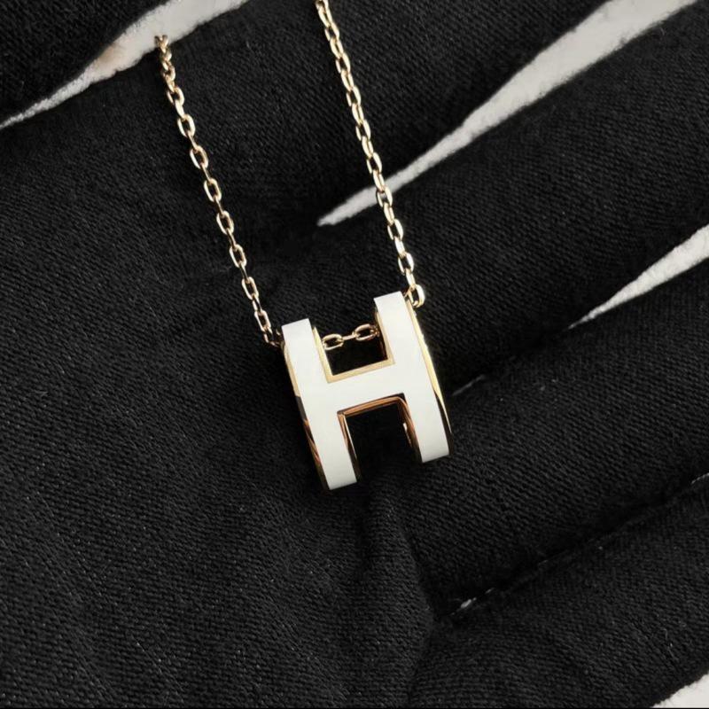 High-End “H” Enamel Pendant Necklace Necklace with a white 'H' pendant on a black fabric background
