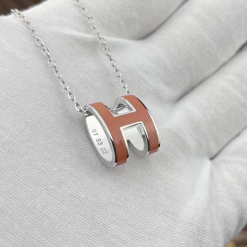 High-End “H” Enamel Pendant Necklace Silver and brown pendant necklace on a light gray fabric background