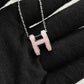 High-End “H” Enamel Pendant Necklace Necklace with a pink 'H' pendant on a black fabric background