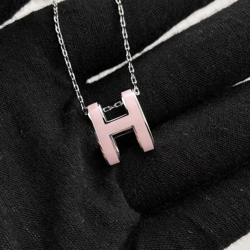 High-End “H” Enamel Pendant Necklace Necklace with a pink 'H' pendant on a black fabric background