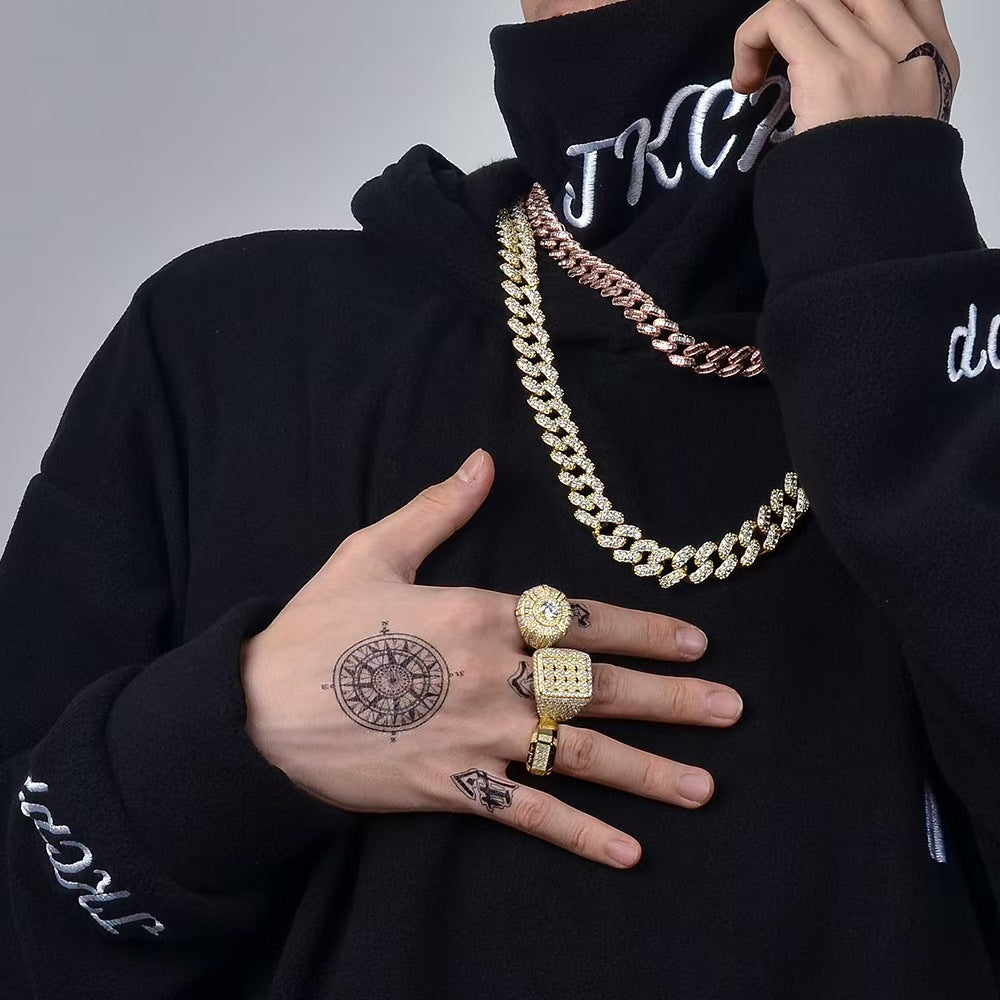 Person wearing a black hoodie with visible branding, gold chain necklace, and rings on a gray background.