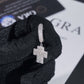 Silver cross-shaped earring held by a gloved hand on a black and white background