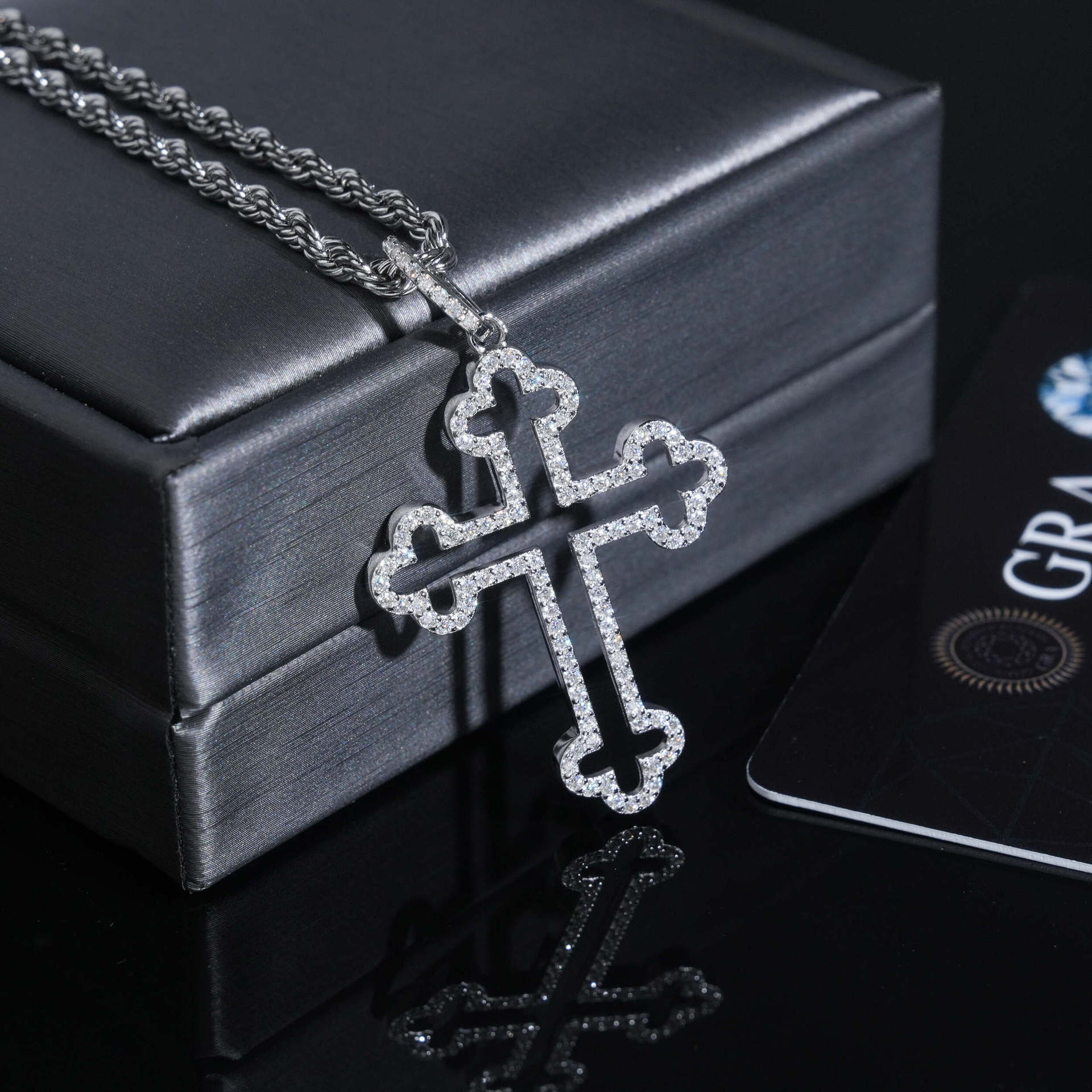 Silver cross necklace on a black box with a card in the background